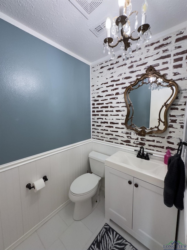 half bath with wainscoting, toilet, a textured ceiling, vanity, and a notable chandelier