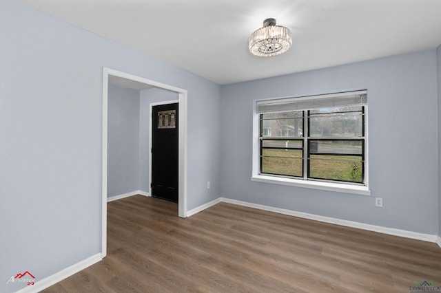 spare room with dark wood-type flooring and a chandelier