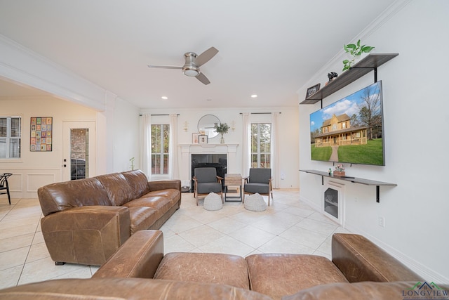 living area featuring light tile patterned flooring, a ceiling fan, a fireplace, and crown molding