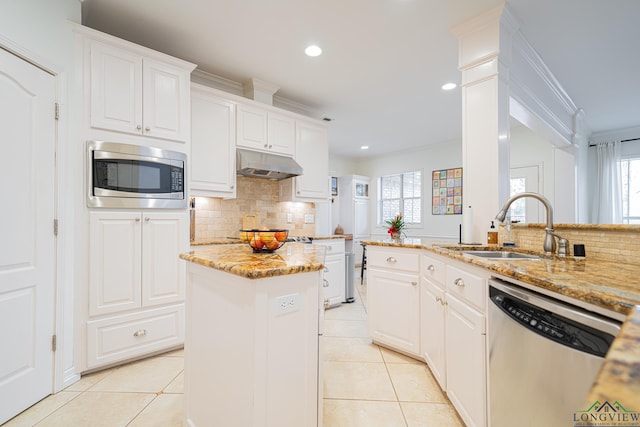 kitchen with under cabinet range hood, a sink, appliances with stainless steel finishes, crown molding, and light tile patterned floors