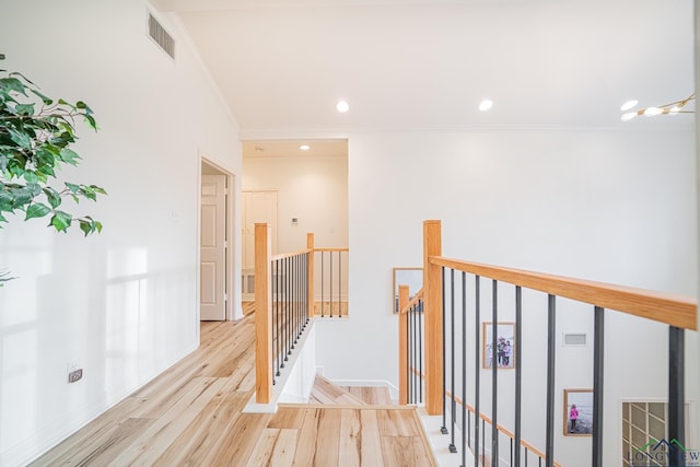 hallway with wood finished floors, an upstairs landing, visible vents, and ornamental molding