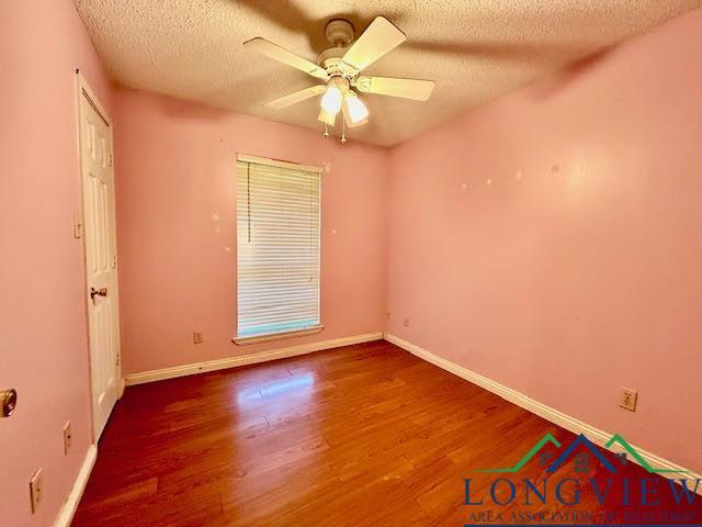 empty room with ceiling fan, wood-type flooring, and a textured ceiling