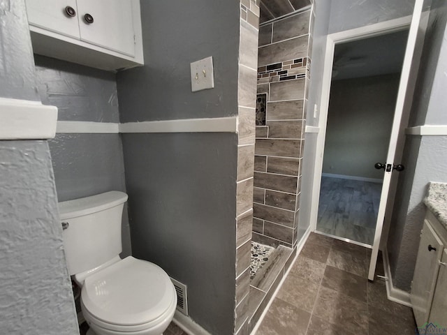 bathroom featuring a tile shower, vanity, and toilet