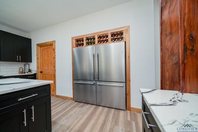 kitchen featuring light stone counters, backsplash, stainless steel fridge, and light wood-type flooring