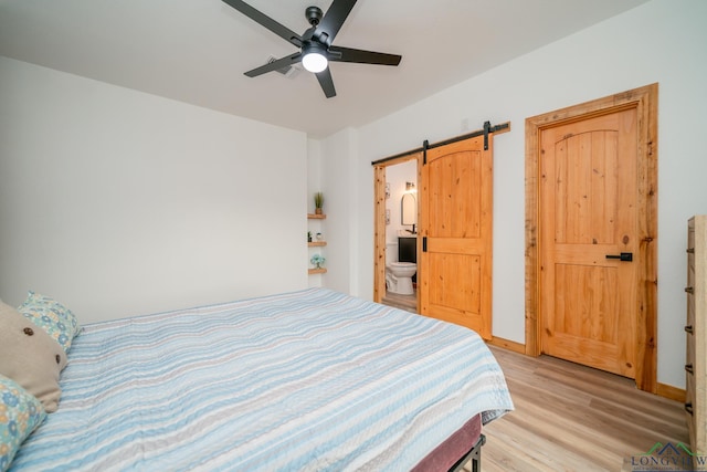 bedroom with ensuite bathroom, a barn door, and light wood-type flooring