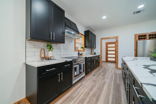 kitchen with light stone counters, stainless steel stove, decorative backsplash, and light hardwood / wood-style flooring