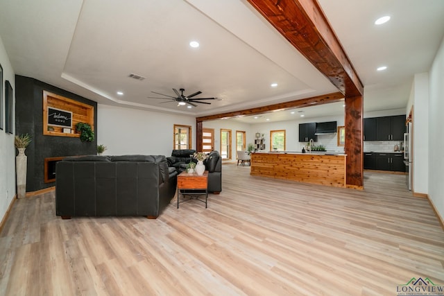 living room featuring ceiling fan, a tray ceiling, and light hardwood / wood-style flooring