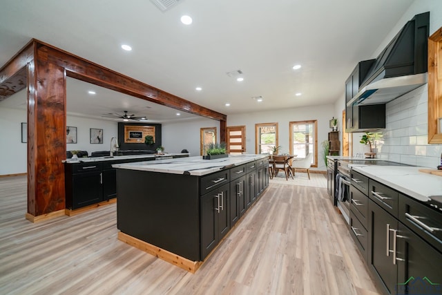 kitchen with tasteful backsplash, light wood-type flooring, a kitchen island, and wall chimney range hood