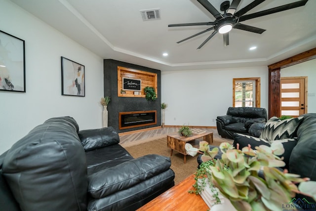 living room with a large fireplace, a raised ceiling, and ceiling fan