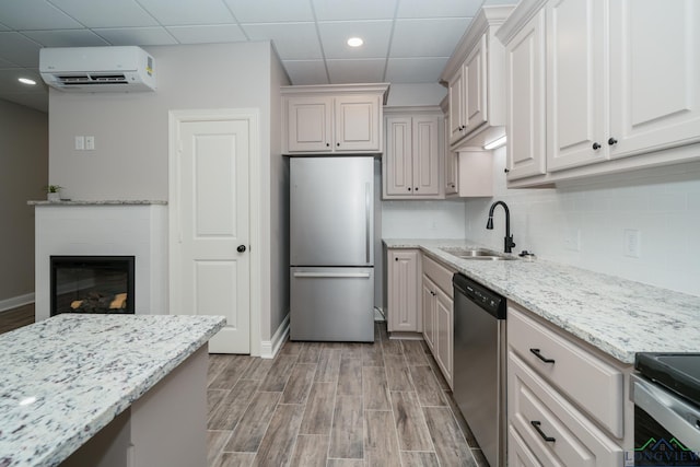 kitchen with a paneled ceiling, light stone counters, stainless steel appliances, a wall unit AC, and sink