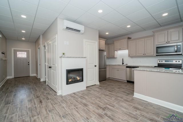 kitchen featuring backsplash, an AC wall unit, sink, appliances with stainless steel finishes, and light stone counters