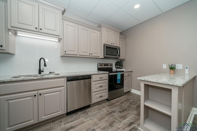 kitchen with light stone countertops, sink, a drop ceiling, and appliances with stainless steel finishes