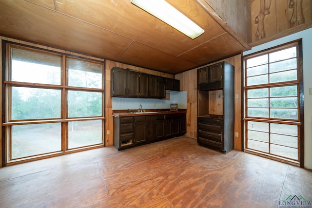 kitchen featuring wood walls, dark brown cabinets, wooden ceiling, and sink