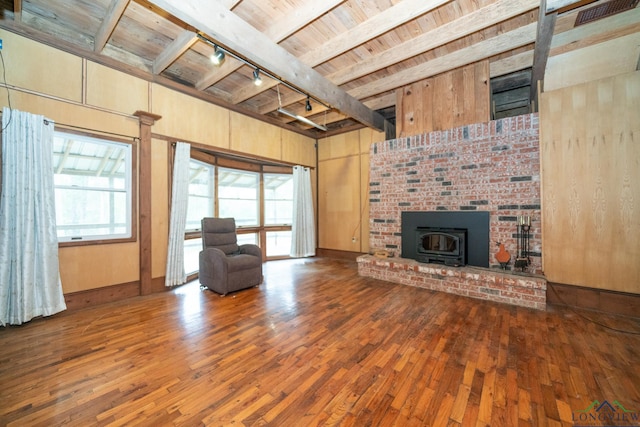 unfurnished living room featuring track lighting, wood ceiling, beam ceiling, hardwood / wood-style floors, and a wood stove