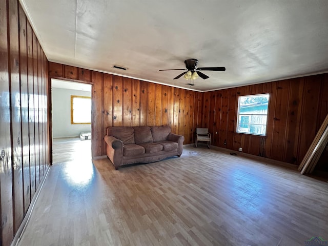 unfurnished living room with light hardwood / wood-style floors, ceiling fan, and wooden walls