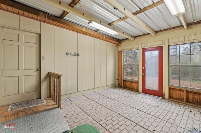 interior space with beam ceiling, brick floor, a wealth of natural light, and wooden walls