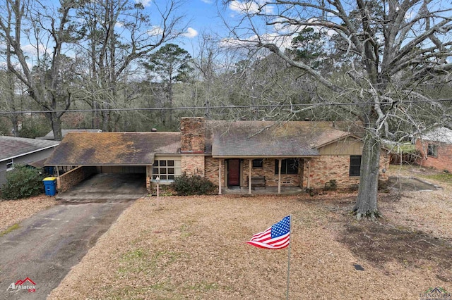 ranch-style house featuring a carport, brick siding, driveway, and a chimney