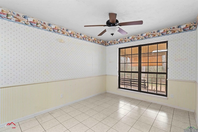 spare room with light tile patterned floors, a ceiling fan, wainscoting, and wallpapered walls