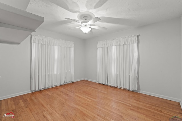 empty room with a textured ceiling, ceiling fan, light wood-type flooring, and baseboards