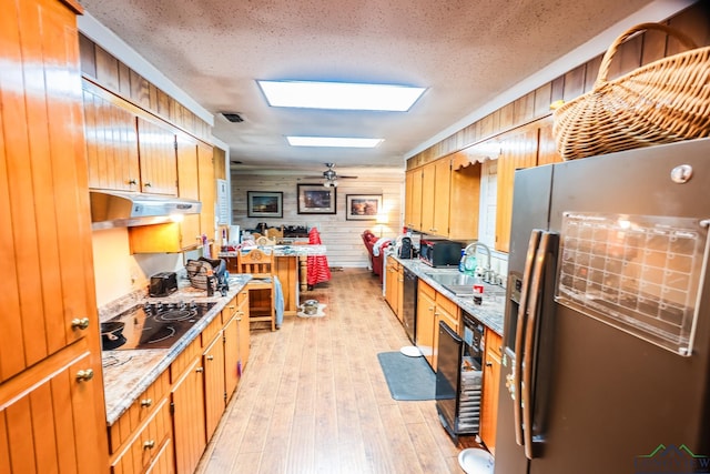 kitchen featuring a skylight, sink, a textured ceiling, wooden walls, and black appliances