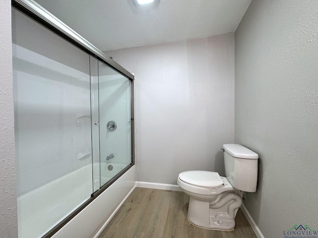 bathroom with hardwood / wood-style floors, shower / bath combination with glass door, and toilet