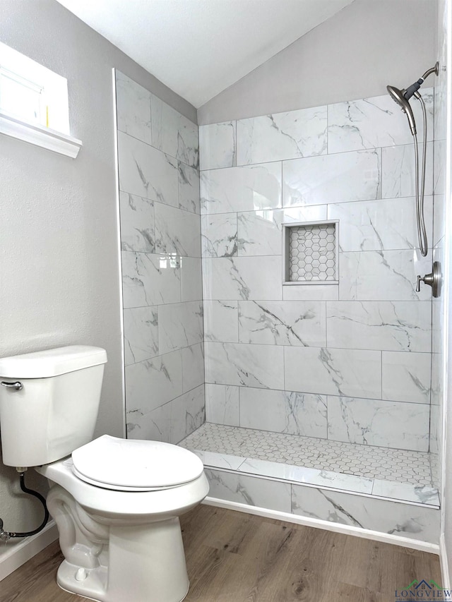 bathroom with a tile shower, lofted ceiling, hardwood / wood-style floors, and toilet