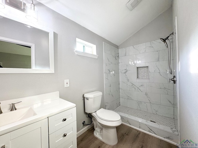 bathroom featuring lofted ceiling, tiled shower, vanity, wood-type flooring, and toilet