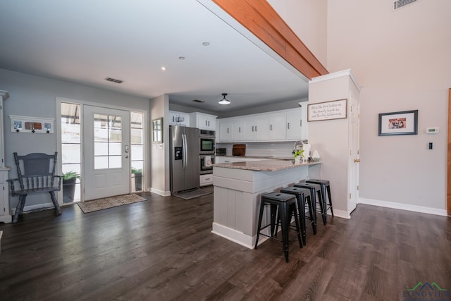 kitchen featuring white cabinets, a kitchen breakfast bar, stainless steel fridge, light stone countertops, and kitchen peninsula