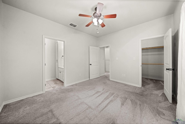 unfurnished bedroom featuring ceiling fan, light colored carpet, a walk in closet, and ensuite bath