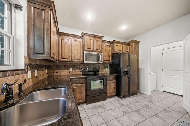 kitchen featuring sink, washer / clothes dryer, dark stone counters, decorative backsplash, and black appliances