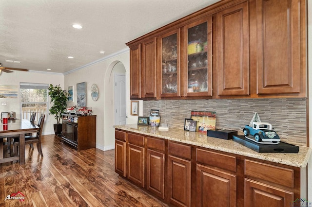 kitchen featuring tasteful backsplash, ornamental molding, light stone countertops, and dark hardwood / wood-style flooring