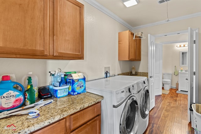 laundry area featuring cabinets, washing machine and dryer, ornamental molding, and light hardwood / wood-style flooring