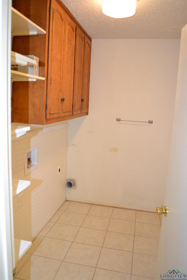 clothes washing area featuring light tile patterned floors, electric dryer hookup, cabinets, washer hookup, and a textured ceiling