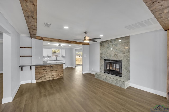 unfurnished living room featuring beam ceiling, ceiling fan, dark hardwood / wood-style flooring, and a high end fireplace