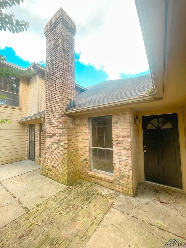 1204-1206 Brandywine, Longview, TX 75601 - view of exterior entry featuring a chimney, brick siding, a patio, and a shingled roof