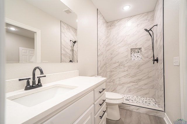 bathroom featuring tiled shower, toilet, vanity, and hardwood / wood-style flooring