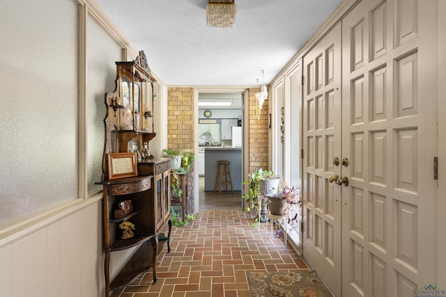corridor featuring brick floors, a textured ceiling, and brick wall