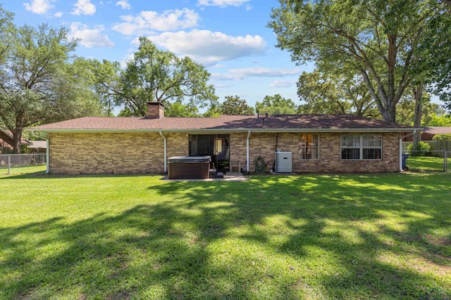 rear view of house with a hot tub, a chimney, brick siding, and central air condition unit