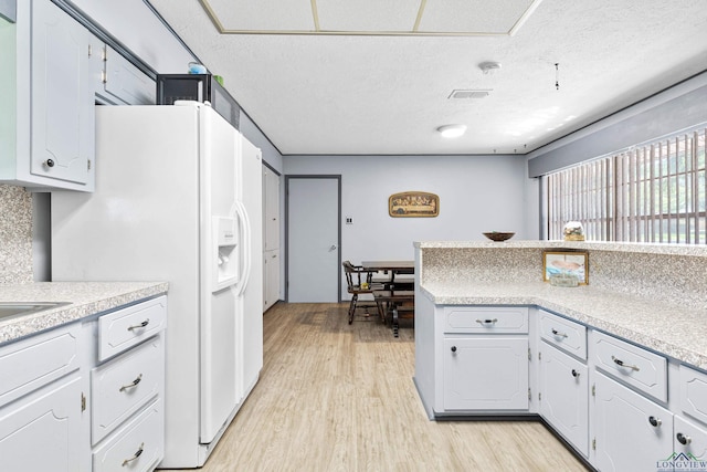 kitchen featuring light wood finished floors, a textured ceiling, light countertops, and white refrigerator with ice dispenser