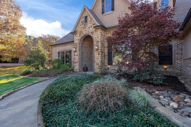 view of front of property with stone siding, brick siding, roof with shingles, and stucco siding