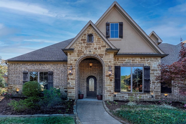 view of front of property with stone siding, roof with shingles, brick siding, and stucco siding