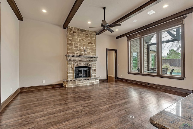 unfurnished living room with a stone fireplace, wood finished floors, a ceiling fan, baseboards, and beam ceiling