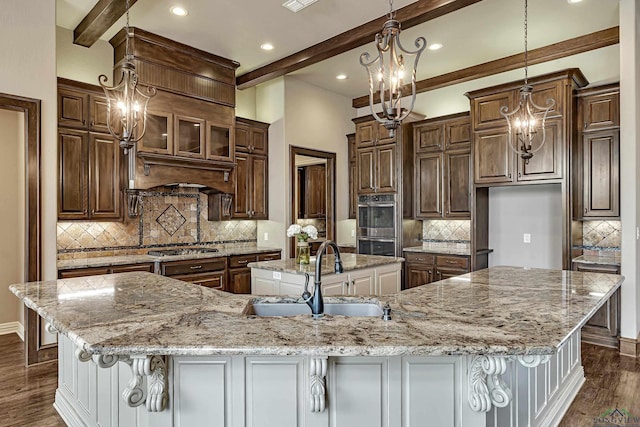 kitchen with dark wood finished floors, beamed ceiling, appliances with stainless steel finishes, a sink, and a large island with sink