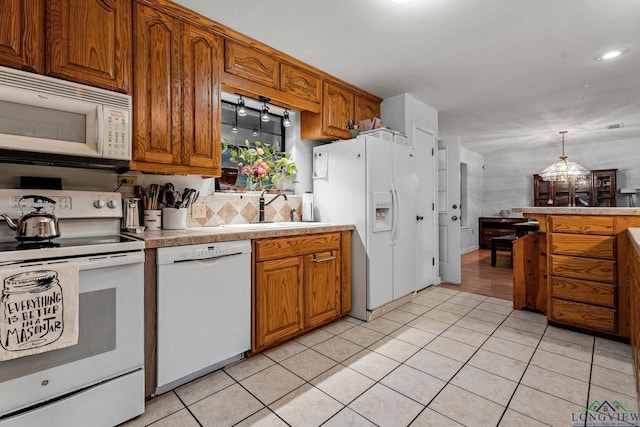 kitchen featuring white appliances, hanging light fixtures, sink, light tile patterned floors, and a chandelier