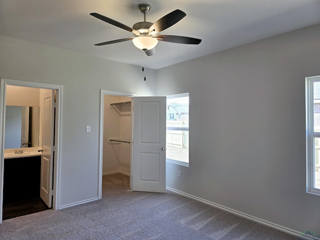 unfurnished bedroom with dark colored carpet, a walk in closet, connected bathroom, and a closet