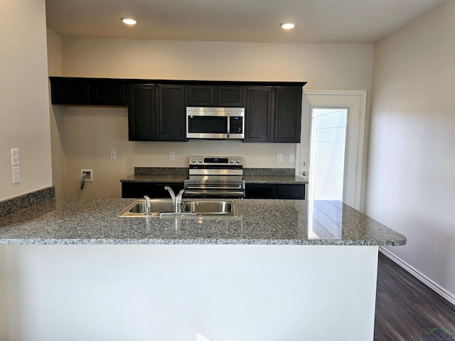 kitchen with appliances with stainless steel finishes, sink, dark hardwood / wood-style flooring, light stone counters, and kitchen peninsula