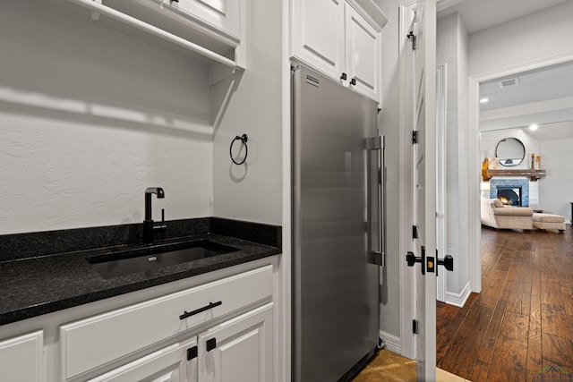 kitchen featuring dark hardwood / wood-style floors, stainless steel refrigerator, white cabinetry, sink, and a brick fireplace