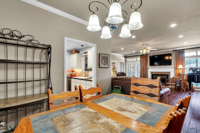 dining room featuring hardwood / wood-style floors, ceiling fan with notable chandelier, sink, ornamental molding, and a fireplace