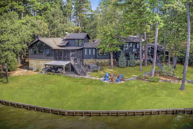 rear view of house with a deck with water view, a yard, a fire pit, and a sunroom