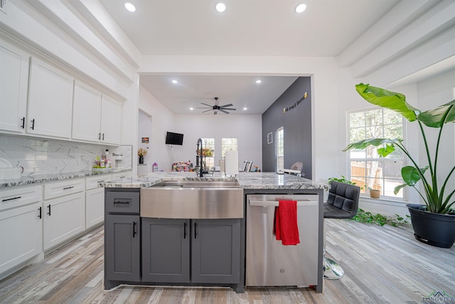 kitchen featuring decorative backsplash, stainless steel dishwasher, ceiling fan, a kitchen island with sink, and white cabinets